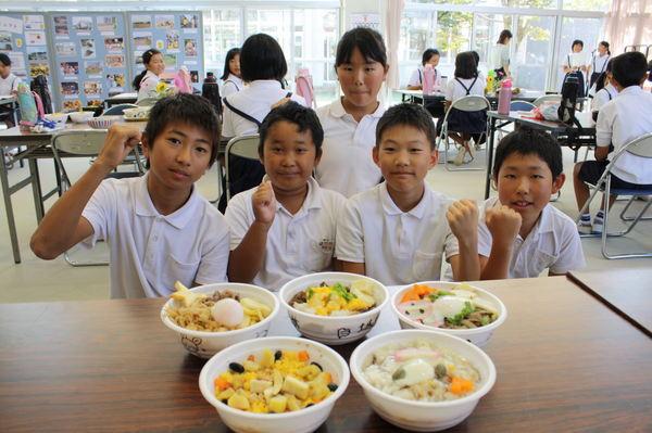 机の上に置かれた、5種類の丼物の後ろでガッツポーズをする小学生の写真